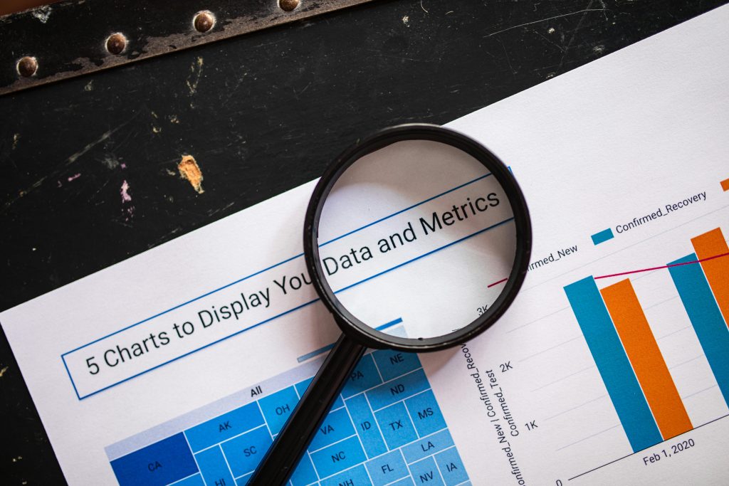 pexels-photo-7947749-7947749 Close-up of a magnifying glass over financial data charts and metrics on printed paper.